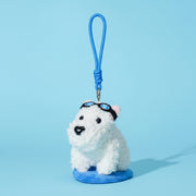 Two plush keychains on a split background, one white dog with sunglasses and blue strap, the other pink and white character with yellow legs and red strap.