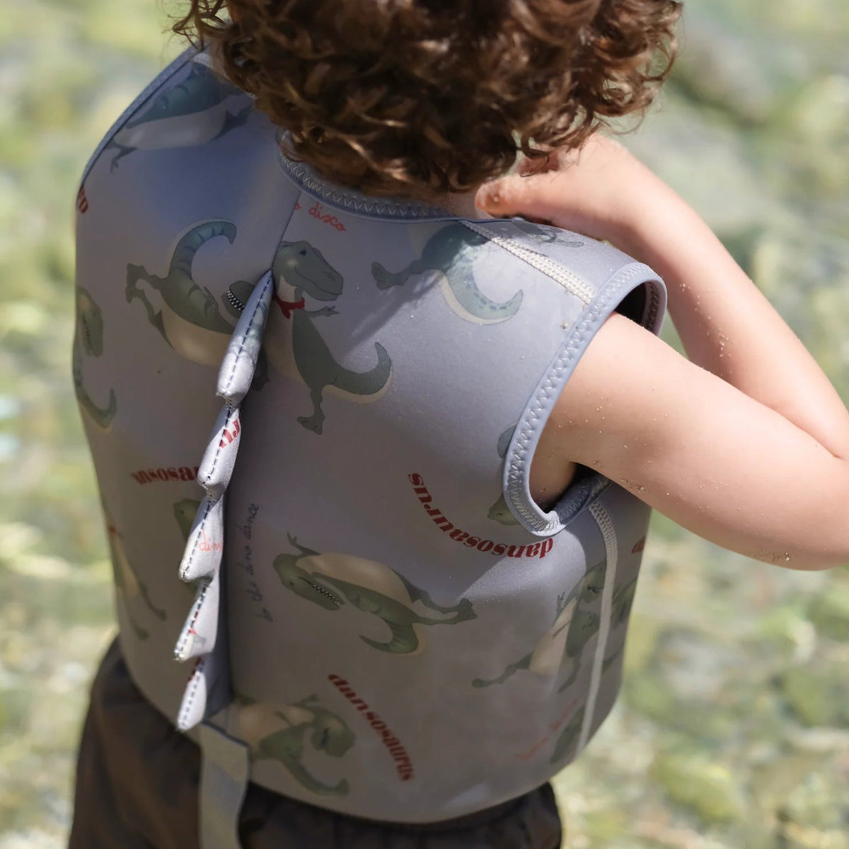 Child wearing a life jacket with dinosaur design by a body of water